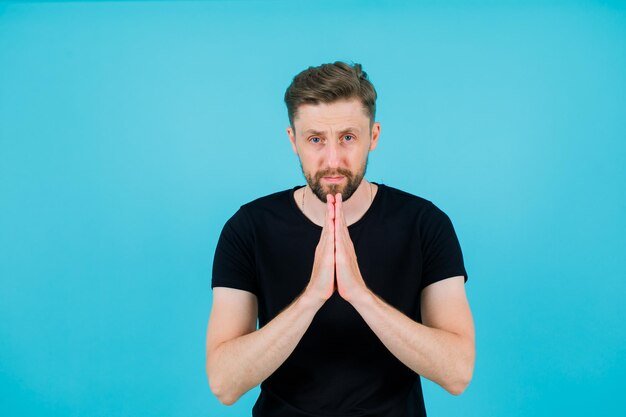 Young boy is looking at camera by holding hands together on blue background