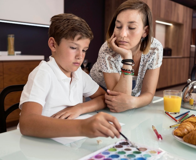 Free photo young boy painting while his mother is checking