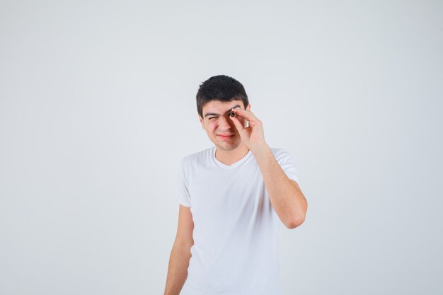 Young boy peeking throug a hole with eurobanknote in t-shirt and looking funny. front view.