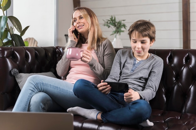 Young boy playing games next to mother on the couch