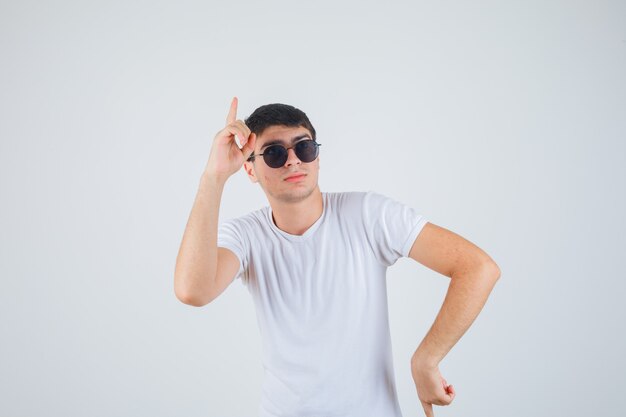 Young boy pointing up in t-shirt and looking confident , front view.