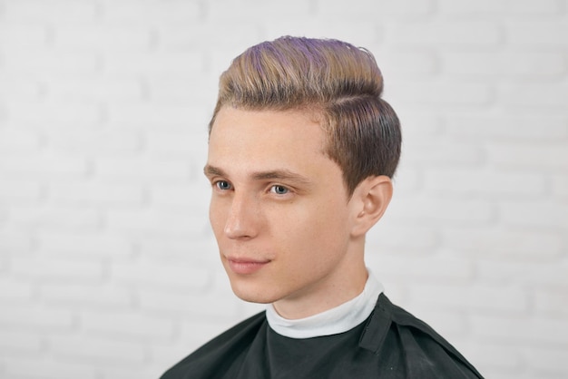 Young boy posing with toned lilac hair on white brick background