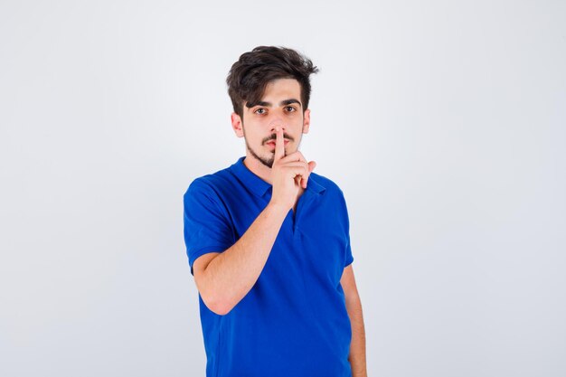 Young boy showing silence gesture in blue t-shirt and looking serious. front view.