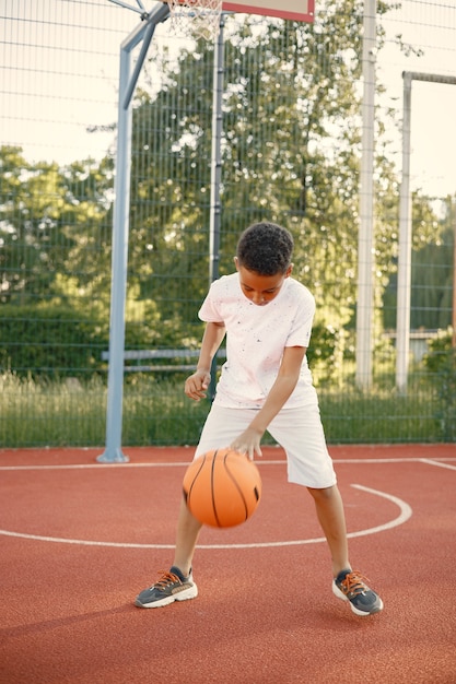 Мальчик стоит на баскетбольной площадке возле парка
