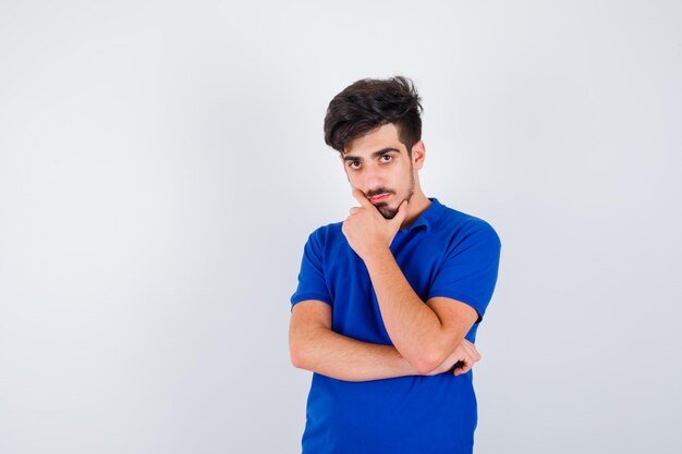 Young boy standing in thinking pose in blue t-shirt and looking pensive. front view.