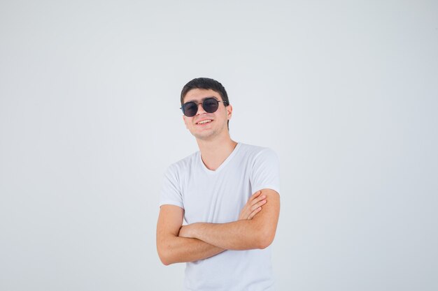 Young boy standing with crossed arms in t-shirt and looking merry , front view.