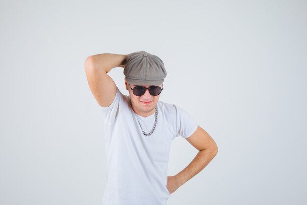 Young boy in t-shirt, hat holding hand behind head and looking thoughtful , front view.