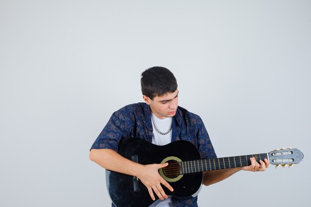 Young boy in t-shirt playing guiter and looking confident , front view.