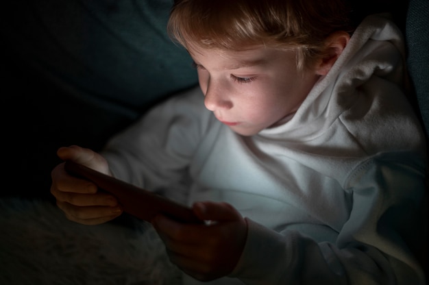 Free photo young boy using smartphone in bed