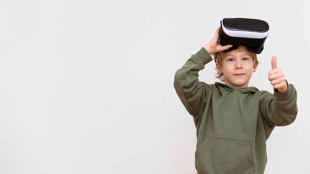 Молодой мальчик с помощью гарнитуры виртуальной реальности и показывает палец вверх