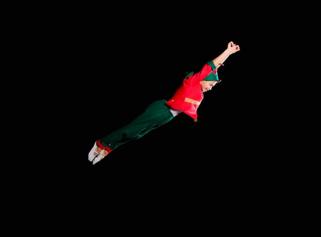 A young boy wearing elf costume is flying. Christmas time, childhood, fairy tale.