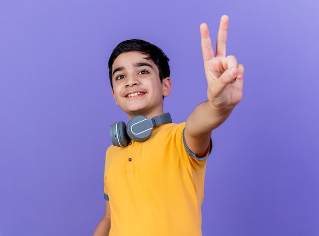 Молодой мальчик в наушниках на шее, изолированном на фиолетовой стене