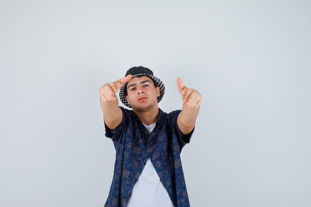 Free photo young boy in white t-shirt, floral shirt, cap showing double thumbs up and looking confident