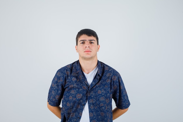 Young boy in white t-shirt, floral shirt holding hands on waist and looking confident