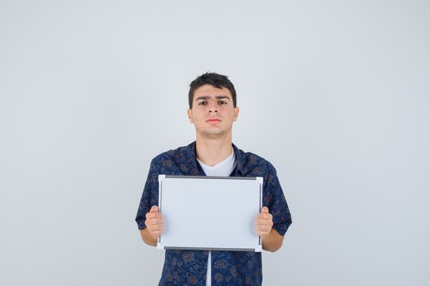 Young boy in white t-shirt, floral shirt holding whiteboard and looking confident