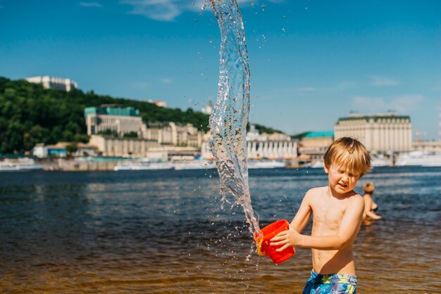 Young boy with eyes closed spills water on sea beach