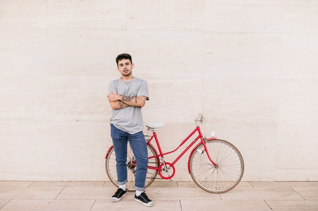 Young boy with folded arms standing near red bicycle