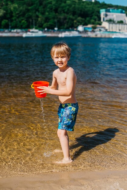 Young boy with naked torso holding bucket on beach