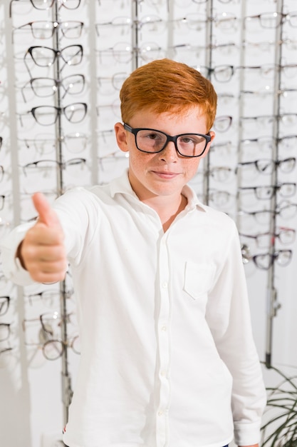 Young boy with spectacle showing thumb up gesture in optics store