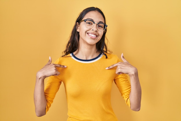 Free photo young brazilian woman wearing glasses over yellow background looking confident with smile on face pointing oneself with fingers proud and happy