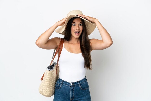 Young brazilian woman with pamela holding a beach bag isolated on white background with surprise expression