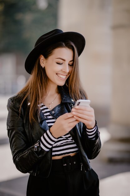 Young brown-haired girl in a leather jacket, black hat on the city promenade