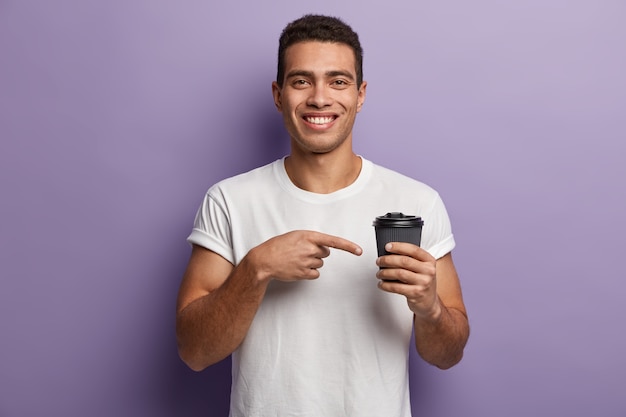 Young brunet man wearing white T-shirt pointing to cup of coffee