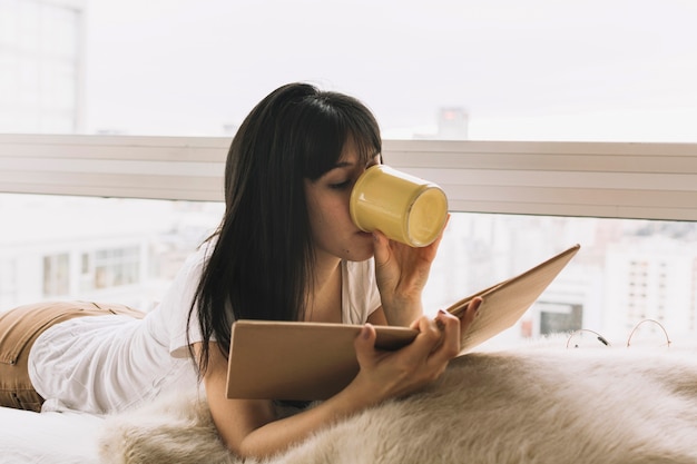 Young brunette drinking and reading on bed