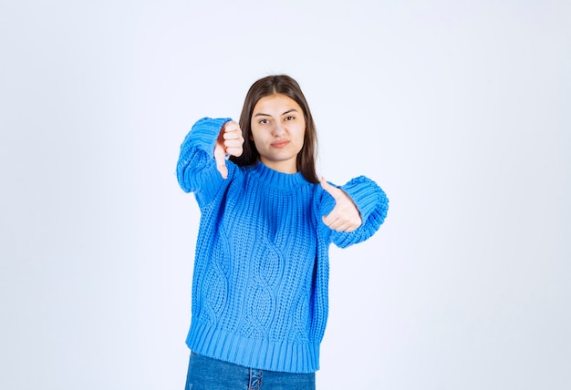 Young brunette girl in blue sweater pointing something on white.