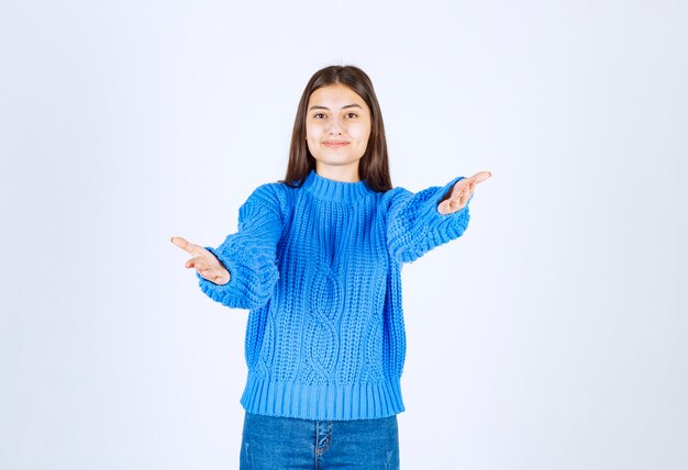 Giovane ragazza castana in maglione blu che posa felicemente su bianco.