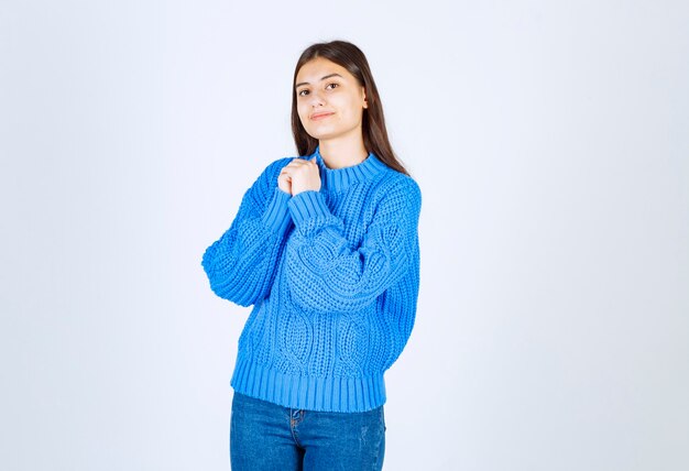 Young brunette girl in blue sweater standing on white.