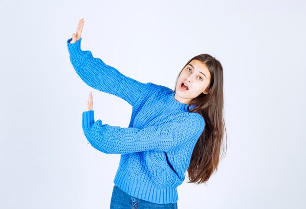 Young brunette girl in blue sweater telling stop to something on white.