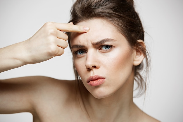 La giovane ragazza castana ha dispiaciuto della sua pelle del fronte dell'acne di problema sopra fondo bianco. cosmetologia della salute e cura della pelle.