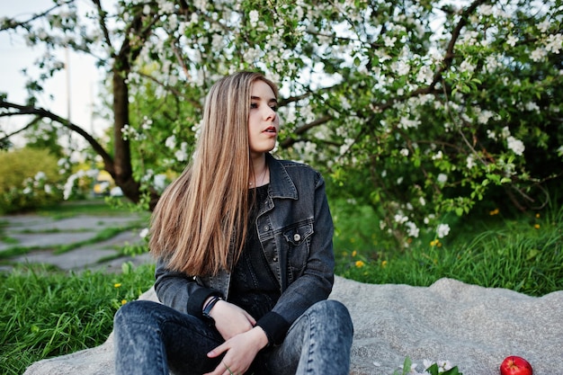 Giovane ragazza bruna in jeans seduto sul plaid contro l'albero del fiore di primavera