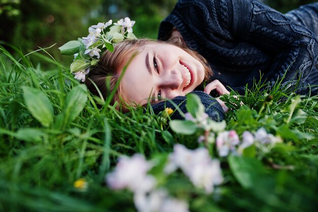 Young brunette girl lying on green grass with branches of blossom tree