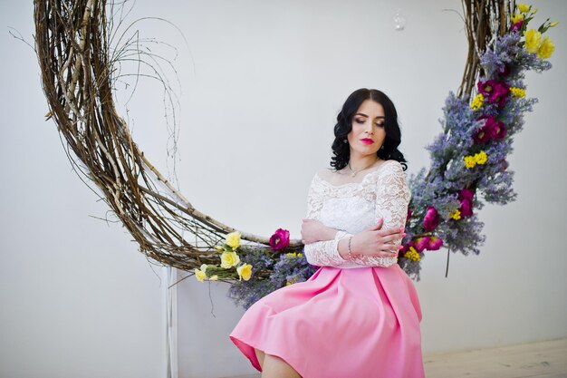 Young brunette girl in pink skirt and white blouse posed indoor against large decorated wreath