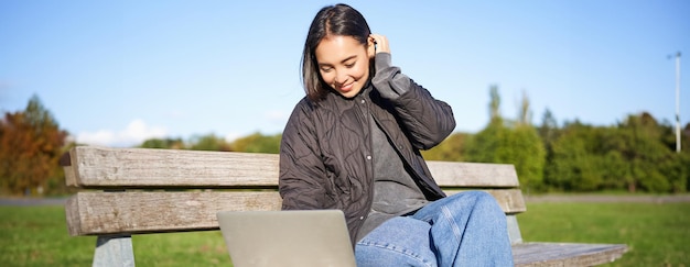 無料写真 若い茶色の女の子がパソコンで公園に座ってビデオを見たり ⁇ インターネットを ⁇ 覧したり ⁇ 屋外で休んでいます ⁇