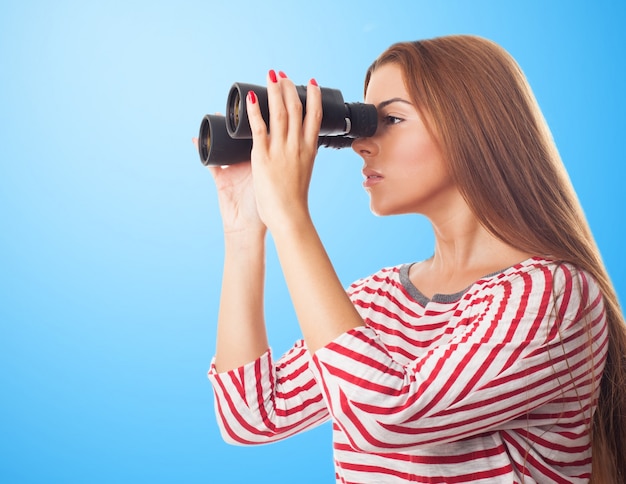 Young brunette girl in striped shirt spying through binoculars