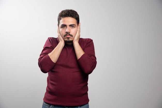 A young brunette man covering his ears and posing .