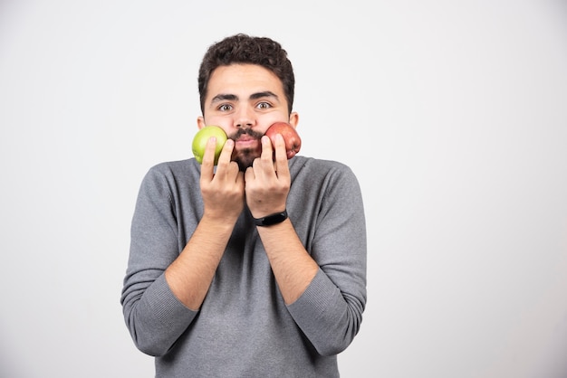 Young brunette man holding apples close to his face.