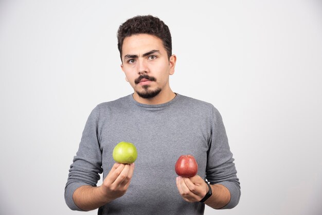 Young brunette man holding two apples on gray.