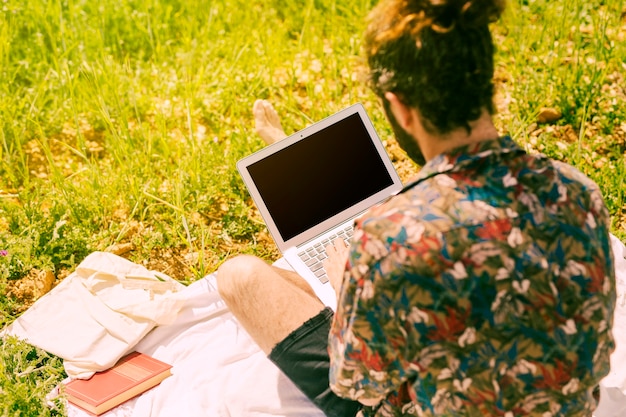 Free photo young brunette man keeping laptop in meadow