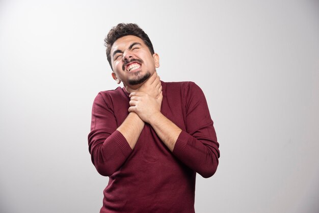 A young brunette man strangling himself over a gray wall.