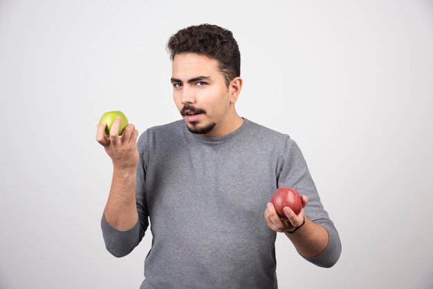 Young brunette man with apples posing on gray.