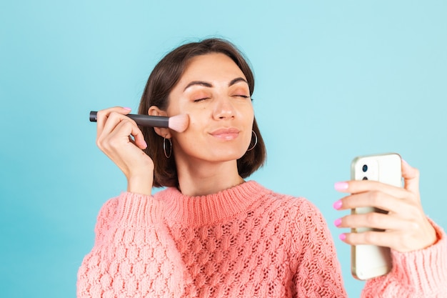 Young brunette in pink sweater isolated on blue wall