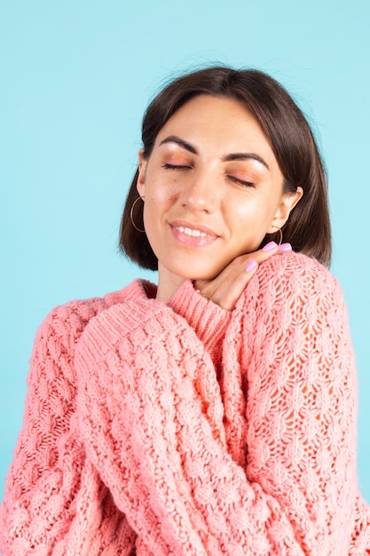 青い壁に分離されたピンクのセーターの若いブルネット