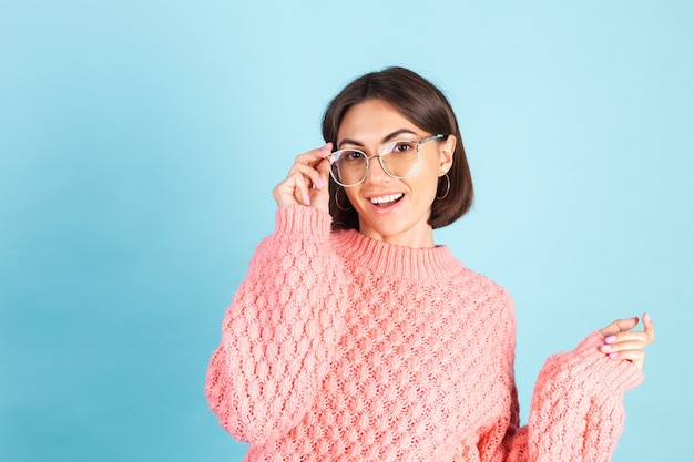 青い壁に分離されたピンクのセーターの若いブルネット