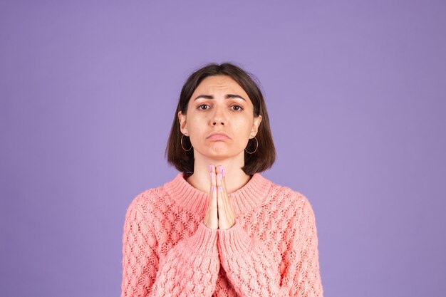 Young brunette in pink sweater isolated on purple wall