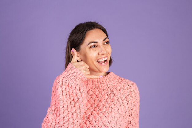 Young brunette in pink sweater isolated on purple wall