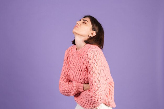 Молодая брюнетка в розовом свитере изолирована на фиолетовой стене